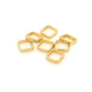 May include: A group of eight gold-coloured metal square jump rings with a hole in each corner. The rings are arranged in a pile on a white background.