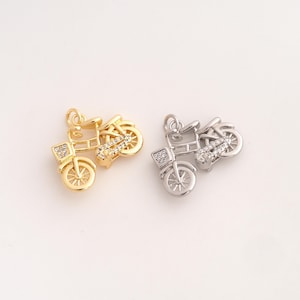 May include: Two bicycle charms, one in a gold tone and one in a silver tone, each featuring a small jump ring at the top, detailed wheel spokes, and clear cubic zirconia stones embedded along the frame and front basket area of the bicycle.