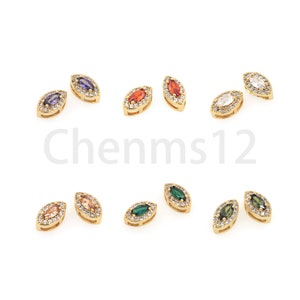 Puede incluir: Pendientes dorados en forma de marquesa, cada uno con una piedra central rodeada de pequeñas piedras claras. Las piedras son de color púrpura, naranja, blanco, melocotón, verde y verde oliva. El texto "Chennms12" es visible.