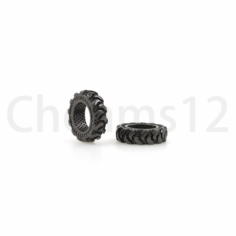 May include: Two black metal tire-shaped beads. The beads are about 1 inch in diameter and have a detailed tread pattern.