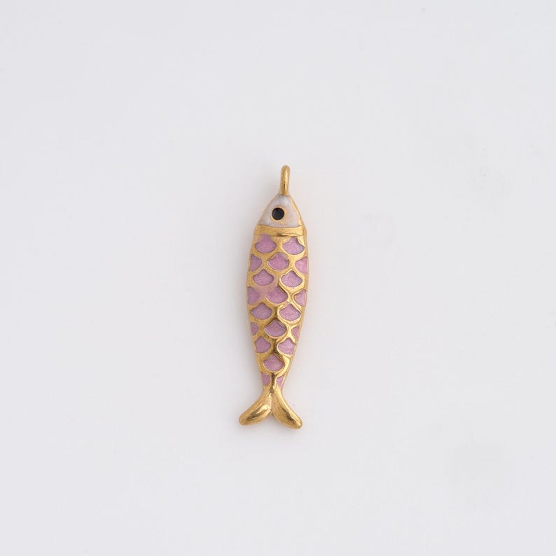 May include: A gold-colored fish pendant with a pink body and gold scale pattern. The fish has a small black eye and a loop at the top for hanging. The pendant is a decorative accessory.