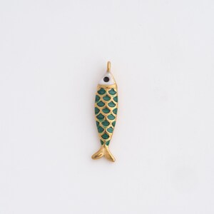 May include: A gold-colored fish pendant with a green scale pattern and a white and black eye. The fish has a small loop at the top for hanging. The pendant is likely made of metal and enamel.