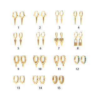 Peut inclure: Quinze paires de boucles d'oreilles créoles dorées avec différents pendentifs, notamment des pointes, des étoiles, des cœurs, des mauvais yeux, des cadenas et des accents turquoise.