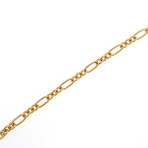 May include: Gold-colored chain necklace with a Figaro link design. The chain features alternating elongated oval links and smaller, circular links. The necklace is displayed against a white background, highlighting its metallic sheen and intricate pattern.