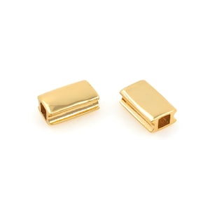 Puede incluir: Dos separadores de cuentas de metal de color dorado, de forma rectangular y con un agujero cuadrado en el centro.
