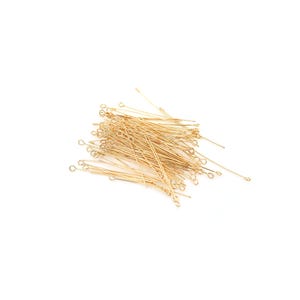 May include: A pile of gold-coloured head pins with a loop at one end. The pins are approximately 2.5 cm long.