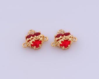 May include: Two gold-colored heart-shaped charms with red gemstone centers. Each charm has a decorative gold filigree design and small clear stones at the top. The charms have loops for attaching to jewelry.