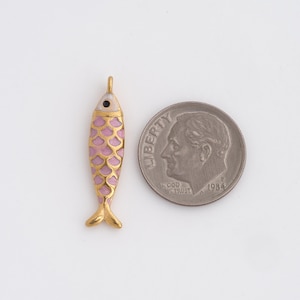 May include: A gold-colored fish pendant with a pink scale pattern and a white head. The fish has a small black eye and is next to a U.S. dime coin for size comparison. The pendant is likely for jewelry making.