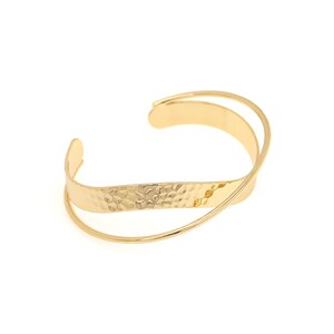 May include: A gold-toned bangle bracelet with a hammered texture and a thin, curved band that wraps around the main band.