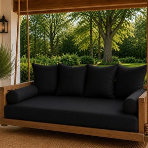 May include: A wooden porch swing bed featuring a natural light brown wood frame suspended by thick tan ropes. The swing includes a large rectangular seat cushion, four square back cushions, and two cylindrical bolster pillows, all in solid black.