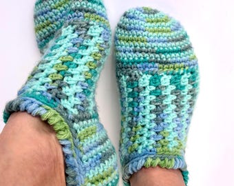 May include: A pair of crocheted slippers in shades of blue, green, and gray. The slippers have a textured pattern and a ruffled edge.