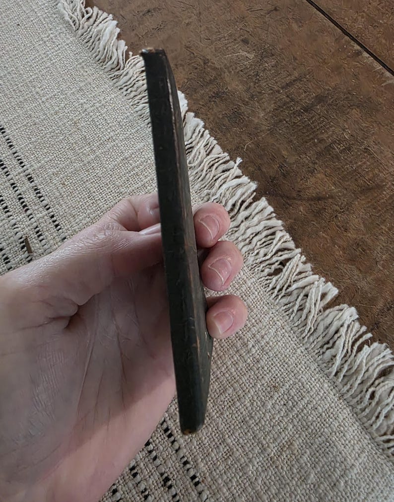 Puede incluir: Un objeto de madera alargado de color marr&oacute;n oscuro, posiblemente una herramienta o una pieza decorativa. El objeto se sostiene en una mano, centr&aacute;ndose en su forma y color. La madera parece envejecida, con una textura ligeramente desgastada.