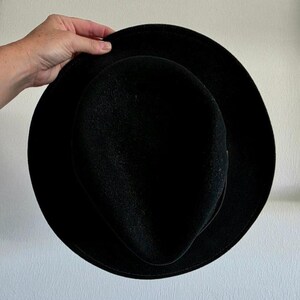 Pu&ograve; includere: Un cappello fedora nero a tinta unita con tesa larga e piatta e corona pizzicata. Il cappello presenta una consistenza liscia simile al feltro e una sottile fascia nera abbinata che circonda la base della corona, per un aspetto uniforme.