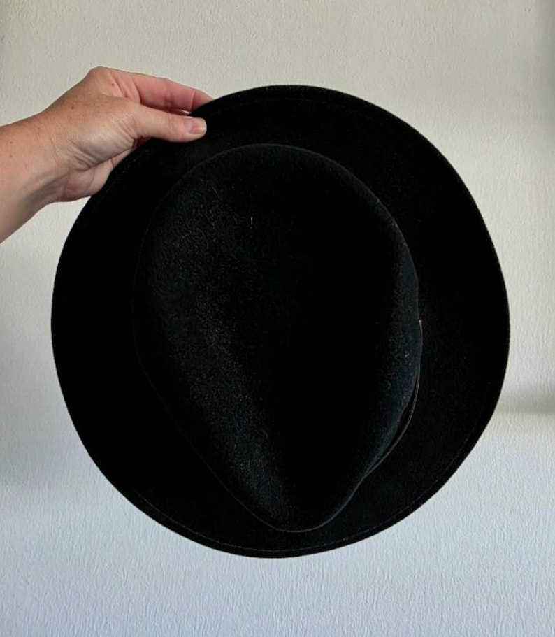 Pu&ograve; includere: Un cappello fedora nero a tinta unita con tesa larga e piatta e corona pizzicata. Il cappello presenta una consistenza liscia simile al feltro e una sottile fascia nera abbinata che circonda la base della corona, per un aspetto uniforme.