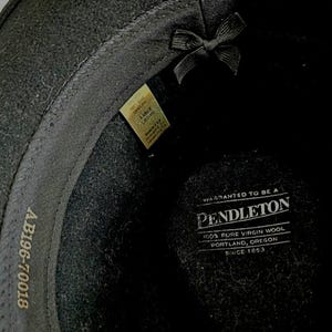 Pu&ograve; includere: L'interno di un cappello nero con un'etichetta Pendleton che recita Warranted to be a Pendleton 100% Pure Virgin Wool Portland, Oregon Since 1863. Una piccola etichetta indica la taglia Large e il codice AB196-70018 &egrave; stampato sulla fascia interna.