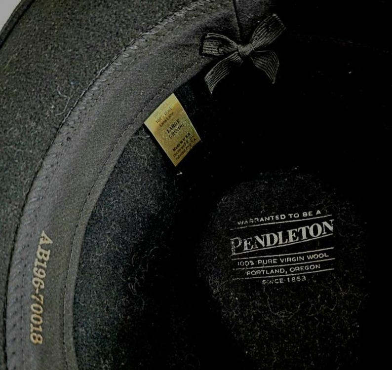 Pu&ograve; includere: L'interno di un cappello nero con un'etichetta Pendleton che recita Warranted to be a Pendleton 100% Pure Virgin Wool Portland, Oregon Since 1863. Una piccola etichetta indica la taglia Large e il codice AB196-70018 &egrave; stampato sulla fascia interna.