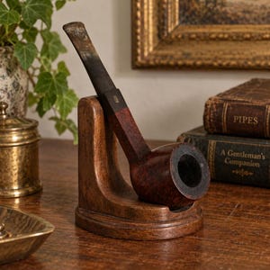 May include: A dark brown wooden tobacco pipe with a smooth, rounded bowl and a straight, tapered stem, resting securely in a matching curved wooden stand. The pipe features a dark, polished finish and a distinct transition from the bowl to the stem.