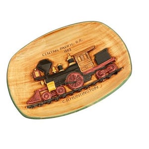 May include: A decorative, oval-shaped dish with a raised relief of a vintage steam train. The train is black, red, and gold, set against a wood-grain background. The dish is trimmed with a green border and features the text "CENTRAL PACIFIC R.R. 1863" and "C.P. HUNTINGTON".