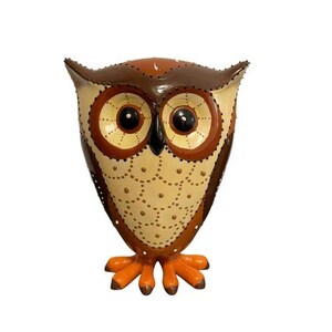May include: A decorative owl figurine with a brown and cream color scheme. The owl has large, round eyes, a black beak, and orange feet. The body is adorned with small, evenly spaced holes.