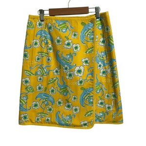 May include: Yellow wrap skirt with a repeating pattern of figures, boats, umbrellas, and flowers in blue and green. The skirt is hanging on a wooden hanger.