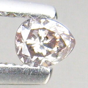 May include: A small, pale pink diamond with a faceted cut. The diamond is held in a pair of tweezers.