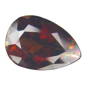 Könnte beinhalten: Ein facettierter, birnenförmiger Edelstein in tiefem Rotbraun. Die Oberfläche des Edelsteins reflektiert das Licht und zeigt klare und dunkle Facetten. Geeignet für Schmuck.