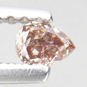 May include: A pear-shaped pink diamond gemstone with a faceted cut. The diamond is held in a pair of tweezers.