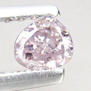 May include: A pale pink diamond with a heart shape, held by a pair of tweezers.