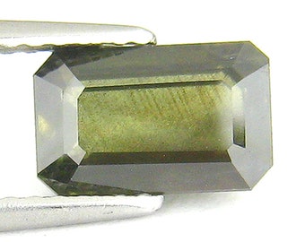 May include: A dark green emerald cut gemstone with a rectangular shape.