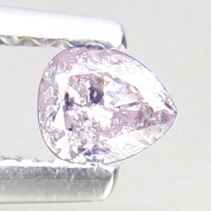May include: A pale pink pear-shaped diamond gemstone held in tweezers.