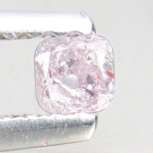 May include: A pale pink, square-shaped diamond with a rough, unpolished finish. The diamond is held in a metal tweezer.
