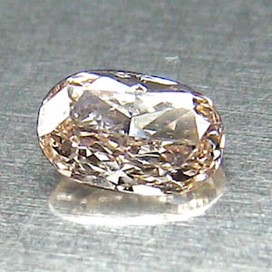 May include: A faceted, oval-shaped diamond with a warm, champagne color. The gemstone reflects light, showcasing its many facets and internal structure. The diamond sits on a reflective surface, enhancing its brilliance.