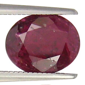 Puede incluir: Una piedra preciosa ovalada de color rojo oscuro con un corte facetado.