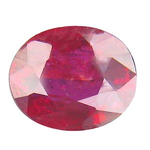 Pode incluir: Uma pedra preciosa facetada de formato oval com uma cor vermelha profunda e vibrante. A pedra apresenta múltiplas facetas geométricas que refletem a luz, criando uma aparência brilhante com vários tons de carmesim e magenta na superfície.