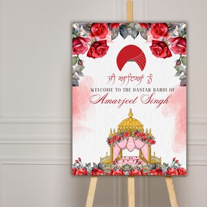 May include: A welcome sign for a Dastar Bandi ceremony, featuring a red turban, a golden canopy, and red roses. The sign reads "Welcome to the Dastar Bandi of Amarjeet Singh" in English and Punjabi.
