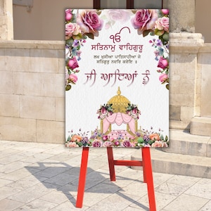 May include: A white sign with pink and gold floral decorations. The sign has a pink and gold canopy with a golden dome on top. The sign reads "ੴ ਸਤਿਗੁਰ ਪ੍ਰਸਾਦਿ" in Gurmukhi script. The sign is on a red easel.