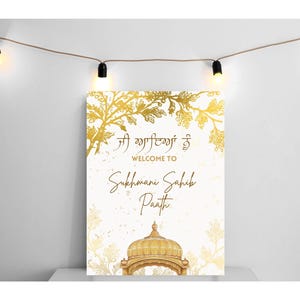 Op de afbeelding: Een gouden welkomstbord met een witte achtergrond en gouden bloemmotieven. Het bord zegt "Welkom bij Sukhmani Sahib Paath" in gouden letters. Het bord heeft ook een gouden illustratie van een Sikh-tempel.