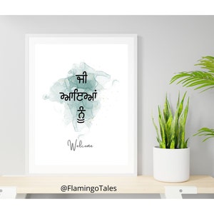 May include: A white framed print with a watercolor background in shades of blue and green. The print features the Punjabi phrase "Aap ka swagat hai" which translates to "Welcome" in English. The print also includes the text "Welcome" and the social media handle "@FlamingoTales".