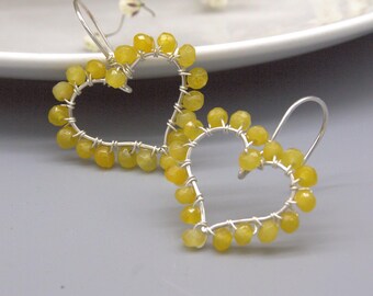 May include: A pair of heart-shaped earrings crafted from silver-toned wire wrapped with small, faceted, translucent yellow beads. Each earring features a simple hook closure and a delicate open-frame design, showcasing the bright yellow stones.