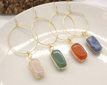 May include: Four pairs of gold hoop earrings with a dangling rectangular stone. The stones are pink, green, orange, and blue.