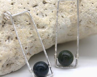 May include: A pair of silver earrings with a dark green and black bead in each. The earrings are made of hammered silver wire and have a rectangular shape.