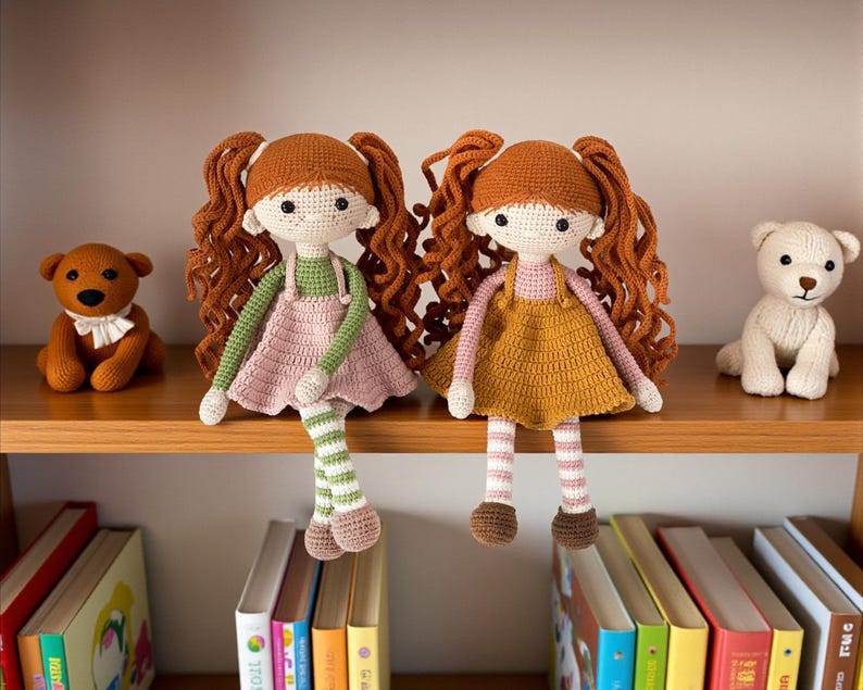 May include: Two handmade crochet dolls with red hair and dresses, one pink and one mustard yellow, sit on a wooden shelf. A brown teddy bear and a white teddy bear are also on the shelf. Books are visible below the shelf.