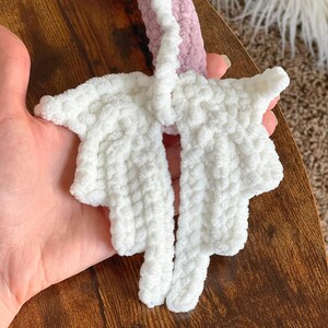 May include: A white crocheted unicorn horn with a pink crocheted base. The horn is made of soft, fluffy yarn and has a pointed tip.