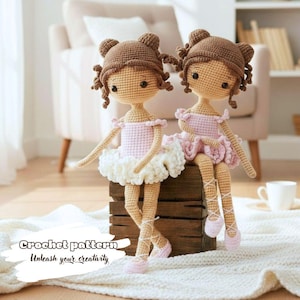 May include: Two handmade crochet ballerina dolls. Each doll has brown hair styled in buns, wearing pink tutus and ballet slippers. The dolls are sitting on a wooden box. The text "Crochet pattern Unleash your creativity" is visible.