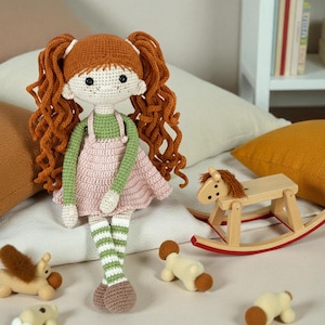 May include: A handmade crochet doll with red hair in pigtails, wearing a green top and pink dress. The doll has striped green and white legs and brown shoes. A wooden rocking horse and small toy animals are in the foreground.