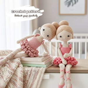 May include: Two handmade crochet ballerina dolls. Each doll wears a pink tutu and ballet shoes. The dolls have light brown hair and are posed on a table with a stack of books and a blanket. The text "Crochet pattern Unleash your creativity" is in the upper left.