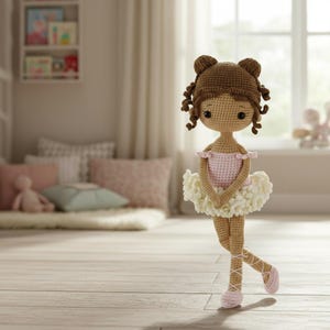 Puede incluir: Mu&ntilde;eca de bailarina de ganchillo hecha a mano. La mu&ntilde;eca tiene cabello casta&ntilde;o peinado en mo&ntilde;os y rizos, y lleva un maillot rosa y un tut&uacute; blanco. La mu&ntilde;eca posa en pointe, con zapatillas de ballet rosas.