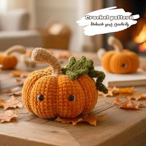 May include: A crocheted orange pumpkin with a beige stem, green leaves, and two black plastic eyes. The text "Crochet pattern Unleash your creativity" is visible in the upper right corner. The pumpkin is surrounded by scattered autumn leaves.