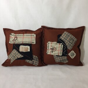 以下が含まれることがあります： 茶色のパッチワークデザインのクッション2つ。ブラウン、ホワイト、ブラック、レッドの様々な格子柄の生地を使用しています。