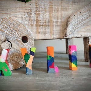 May include: The name "KYLIE" spelled out in colorful, multi-colored crayon letters. The letters are standing on a wooden surface.
